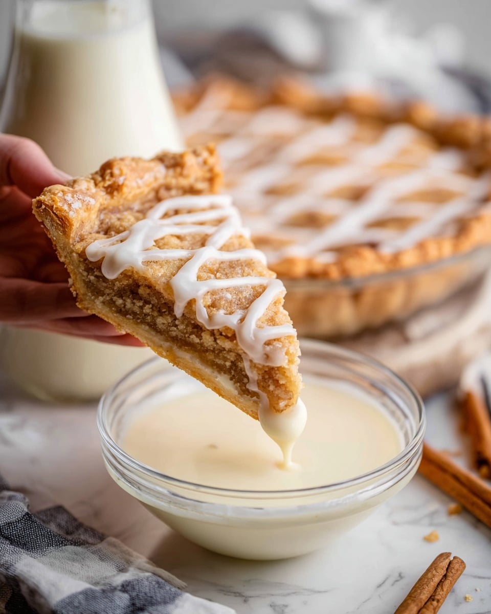 A close-up image shows a single slice of crumbly pie with a light brown texture and a criss-cross pattern of white icing on top, held by a woman's hand as it is dipped into a clear glass bowl filled with creamy white sauce. The pie's crust is golden brown and appears crispy. In the background, a full pie with the same icing pattern is visible, placed on a white marbled surface, along with a glass jug filled with milk and a cinnamon stick nearby. The scene has a soft, warm lighting that highlights the textures and colors. photo taken with an iphone --ar 4:5 --v 7