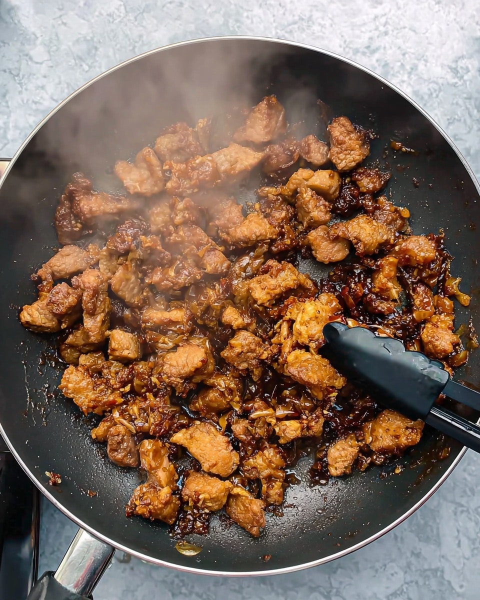 The image shows a black frying pan filled with small pieces of crispy, golden-brown cooked meat being stirred with black tongs. The meat has a crunchy texture with some oily, shiny areas reflecting light. Steam rises gently from the pan, highlighting the heat and freshness of the cooking. The background is a white marbled surface. photo taken with an iphone --ar 4:5 --v 7
