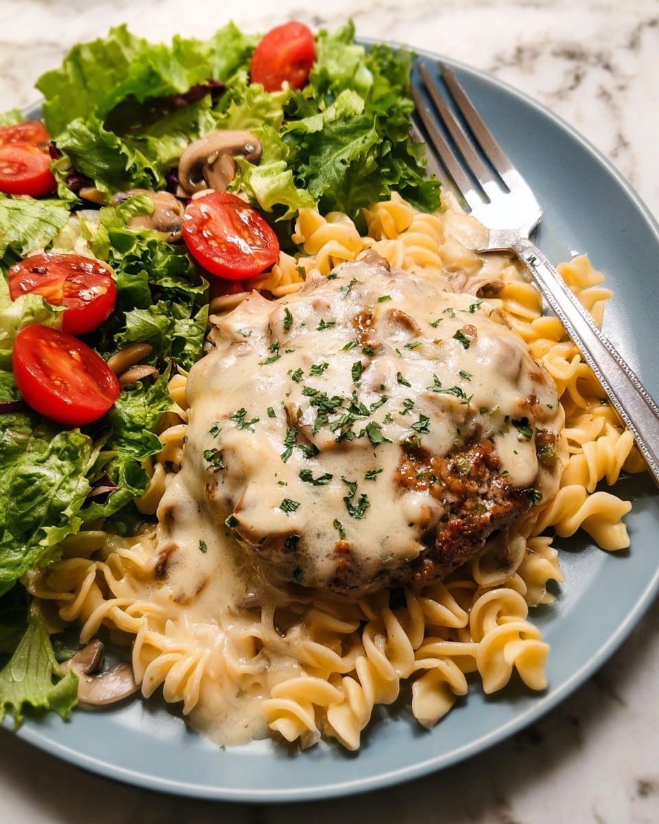 A white plate with a large base layer of creamy light beige pasta with a smooth sauce covering most of it, topped in the center by a thick, browned patty covered with melted cheese and sprinkled green herbs; to the side, a fresh green leafy salad with bright red cherry tomatoes and small pieces of light tan mushrooms. A silver fork rests on the right edge of the plate, all placed on a white marbled surface. Photo taken with an iphone --ar 4:5 --v 7