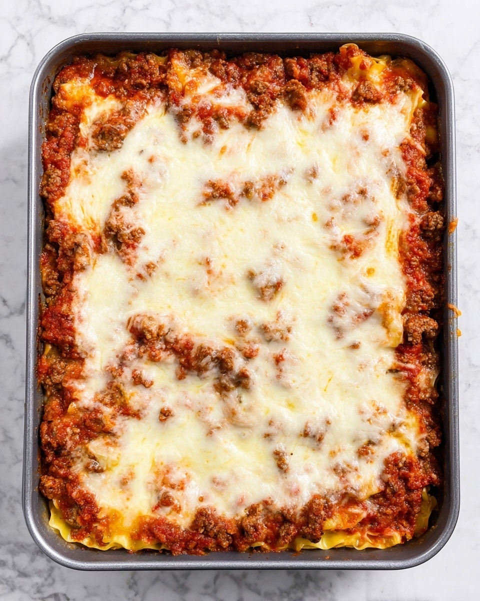 A square baking pan filled with a baked lasagna dish showing four main layers. The bottom layer is a deep red tomato sauce mixed with browned ground meat, creating a textured base around the edges. Above this is a layer of light yellow pasta sheets, mostly hidden but visible near the edges. On top of the pasta, there is another layer of chunky red tomato sauce with bits of browned meat. The top layer is a thick, melted white cheese covering the entire surface with some areas showing a slight golden tint where it has browned in spots. The pan sits on a white marbled surface. photo taken with an iphone --ar 4:5 --v 7