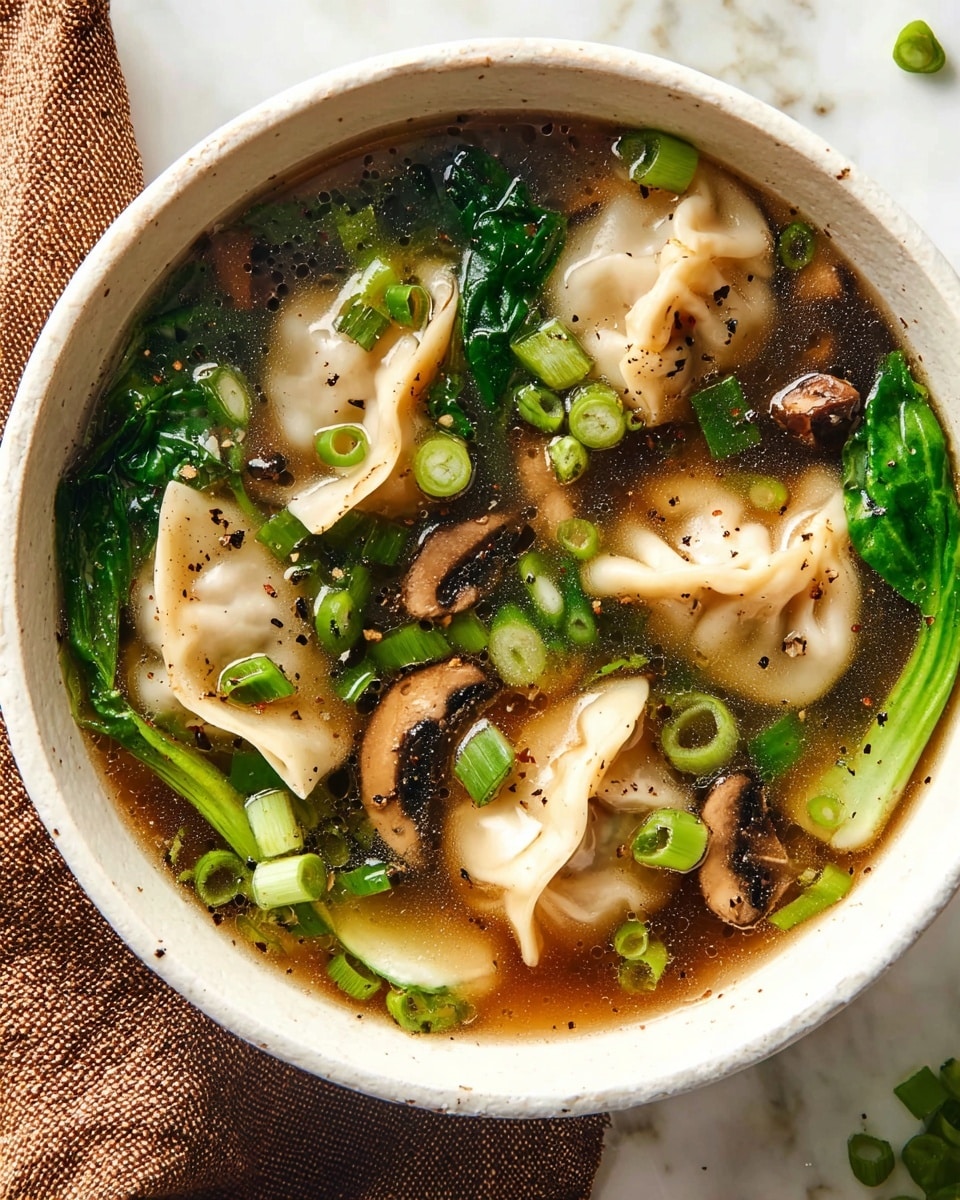 A white bowl filled with clear brown broth holding several pale beige dumplings with soft, wrinkled edges. Around the dumplings, there are bright green chopped spring onions sprinkled on top and fresh leafy green vegetables submerged in the broth. Dark brown, sliced mushrooms float gently among the other ingredients. The broth has small specks of black pepper scattered on the surface. The bowl is set on a white marbled surface, with a brown cloth visible in the corner. photo taken with an iphone --ar 4:5 --v 7