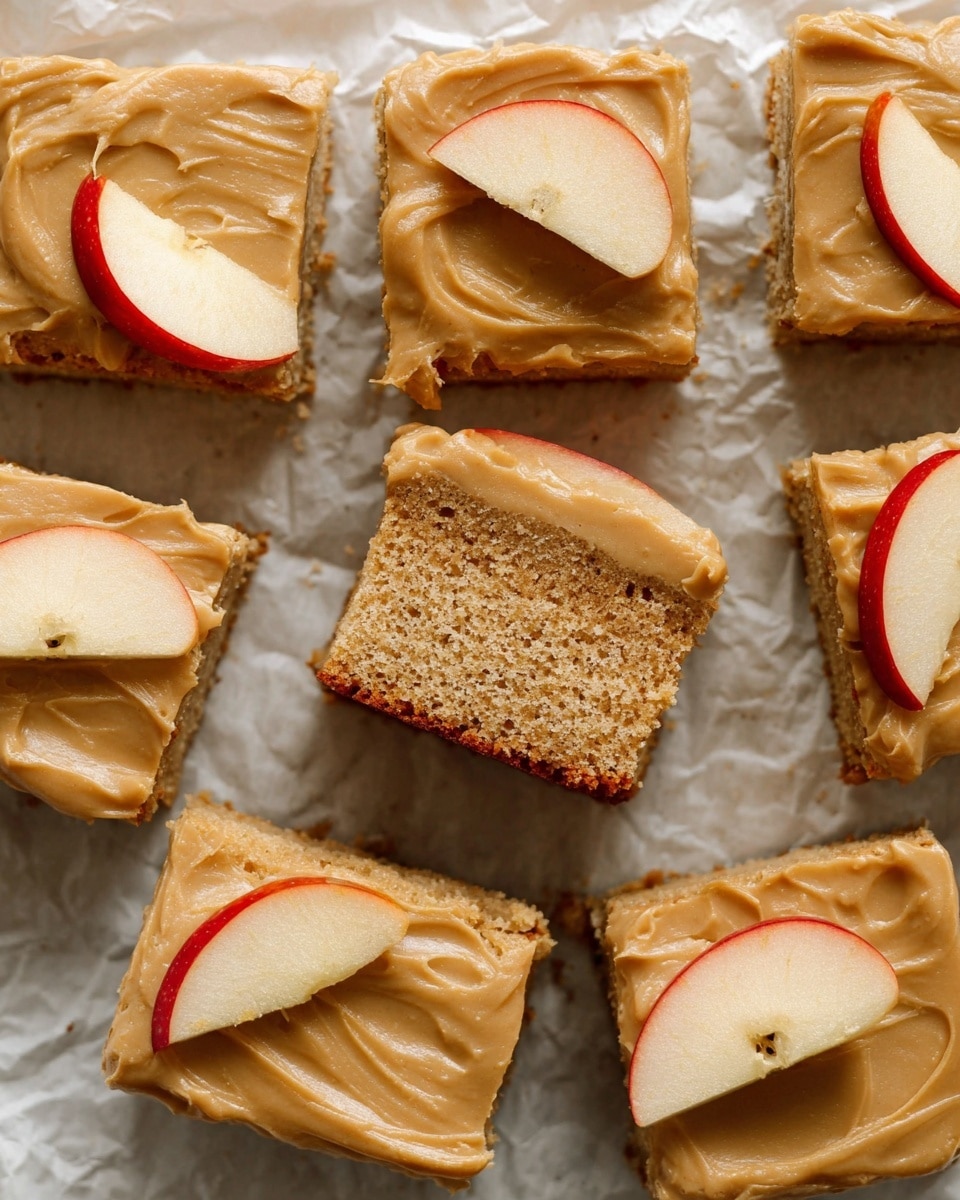 This image shows nine square pieces of cake with two layers each, placed on crumpled white parchment paper over a white marbled surface. The bottom layer is a light brown soft cake with a spongy texture, and the top layer is a smooth, thick caramel-colored frosting spread evenly on each piece. Some squares are topped with thin apple slices that have red skin and a pale yellow inside, neatly placed on one corner. One piece is slightly lifted and angled to highlight its fluffy cake texture and thick frosting layer. The overall look is cozy and homemade with warm tones. photo taken with an iphone --ar 4:5 --v 7