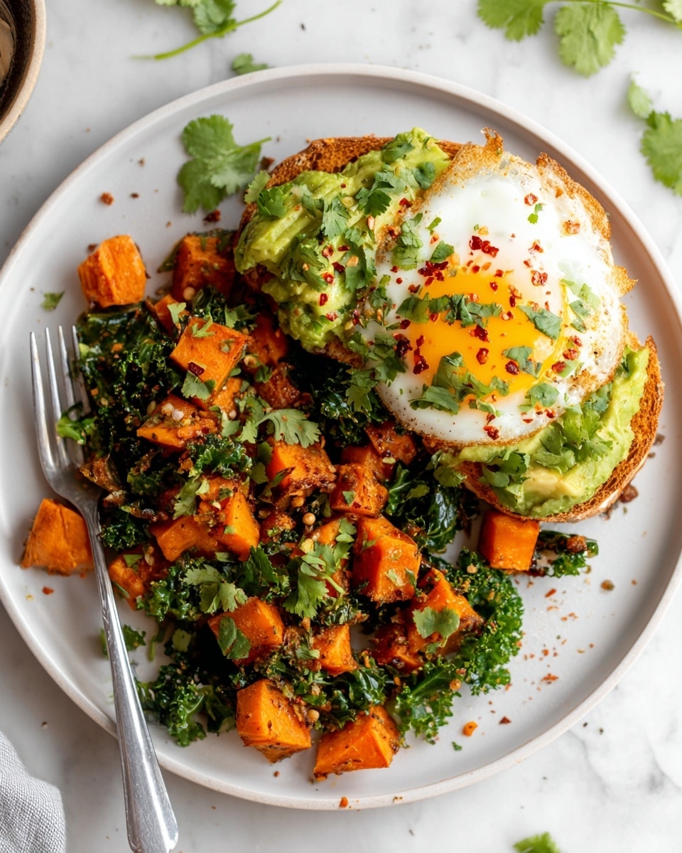 The white plate holds a colorful dish with small orange cubes of cooked sweet potato mixed with green leafy kale spread across most of the plate. Toward the upper right is a slice of toasted bread topped with a layer of mashed avocado, sprinkled with red chili flakes and chopped fresh cilantro. Underneath the avocado is a fried egg with a bright yellow yolk peeking out. A fork rests on the left side of the plate, partly under the sweet potato cubes. The dish sits on a white marbled surface with some scattered leaves around. Photo taken with an iphone --ar 4:5 --v 7