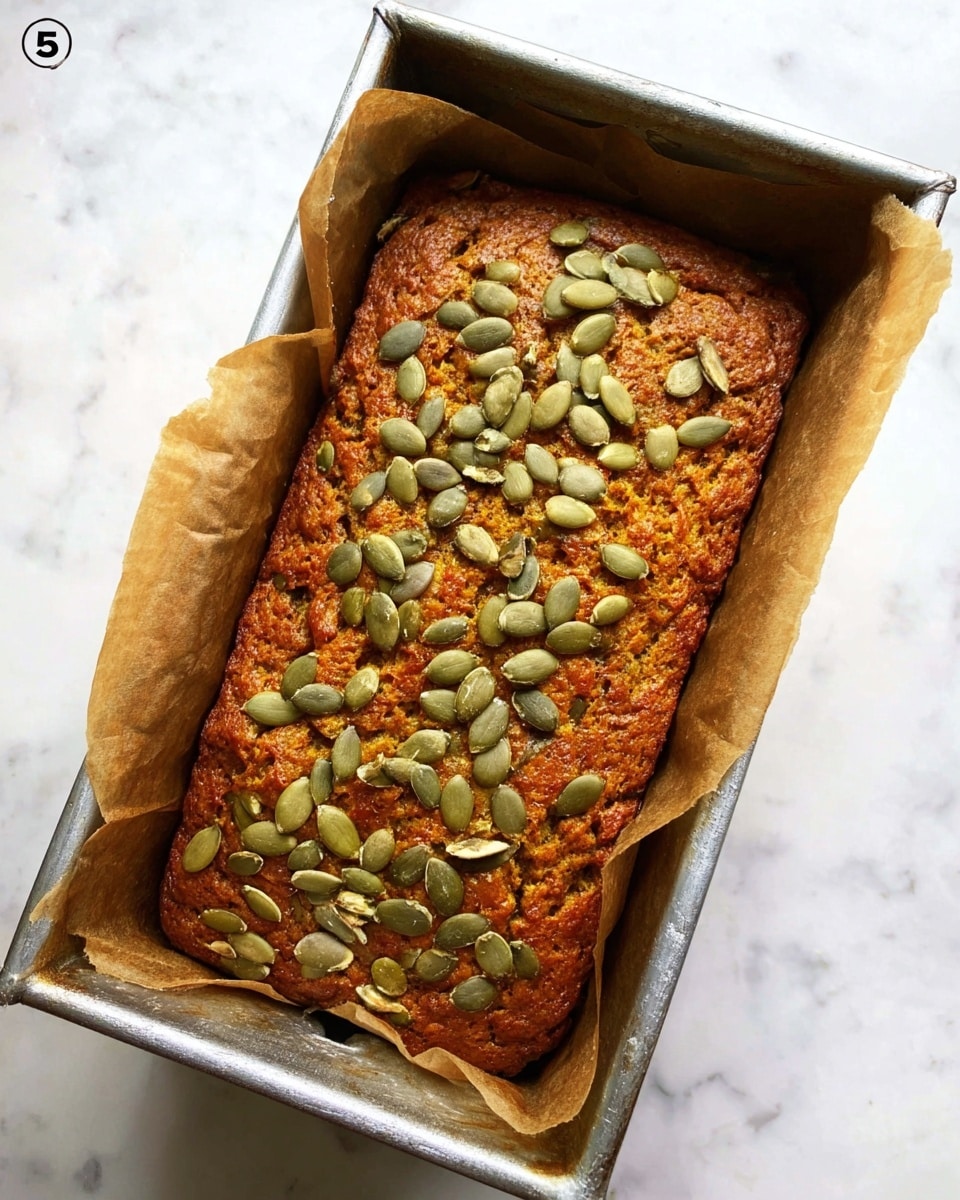 A rectangular loaf of dark orange bread with a rough texture fills a silver metal baking pan lined with brown parchment paper that extends above the pan edges. The top of the bread is sprinkled evenly with pale green pumpkin seeds, some slightly overlapping. The pan sits on a white marbled surface. photo taken with an iphone --ar 4:5 --v 7