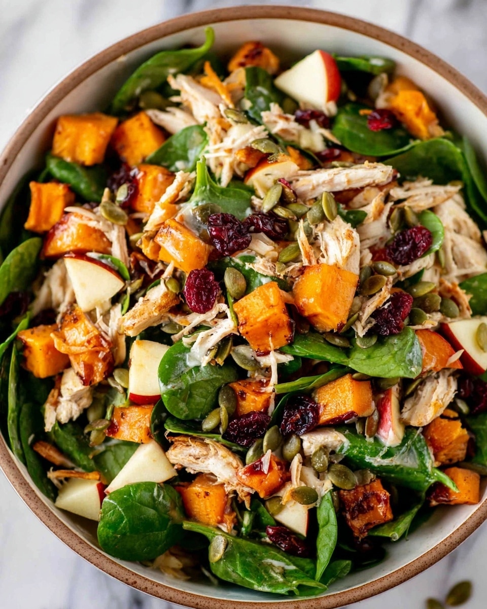 A close-up view of a colorful salad in a white bowl with a brown rim placed on a white marbled surface, showing mixed fresh green spinach leaves as the base layer, topped with shredded light-colored chicken pieces, cubed roasted orange sweet potatoes, small chunks of red-skinned apple with white flesh, dark red dried cranberries, and scattered green pumpkin seeds, all mixed together to create a vibrant, textured, and fresh-looking dish photo taken with an iphone --ar 4:5 --v 7