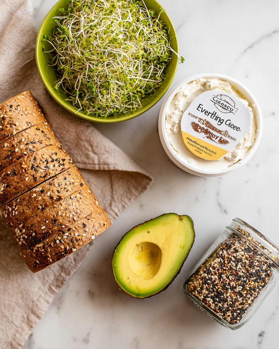 The image shows a white marbled surface with a layered whole grain bread loaf sprinkled with seeds on the left, resting on a beige cloth. Next to it is a halved avocado with bright green skin and creamy yellow-green flesh facing upwards. Above the avocado is a white round container of cottage cheese with a brown and yellow label reading