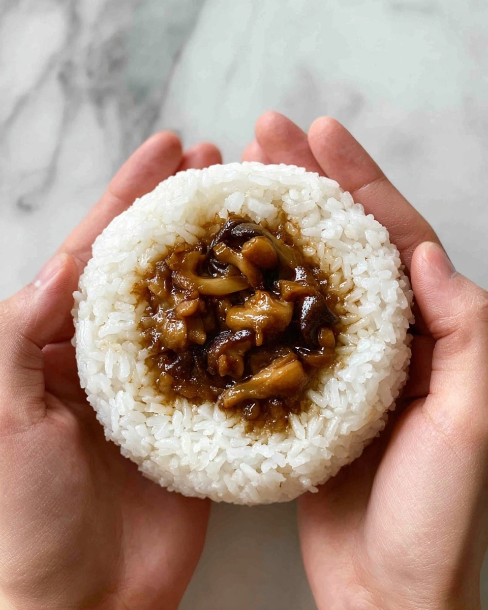 A white ball of sticky rice forms the base layer, shaped smooth and round, with a small hollow filled with a glossy, brown cooked mushroom mixture that is chunky and moist, sitting neatly in the center. The rice is evenly packed and bright white, contrasting with the rich color and texture of the savory filling. The scene is held carefully by a pair of hands against a white marbled surface, showing the details of the rice grains and the shiny sauce on the mushrooms. Photo taken with an iphone --ar 4:5 --v 7
