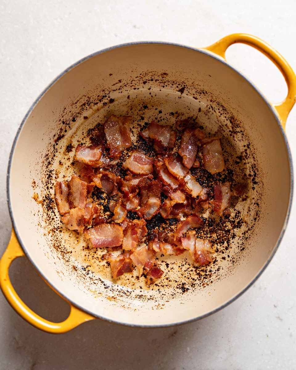 A round white pot with yellow handles holds small pieces of cooked bacon unevenly spread at the bottom. The interior of the pot is off-white with visible brown and black browned bits scattered across the surface, creating a textured, oily look. The pot sits on a white marbled surface, highlighting the rich colors and crisp texture of the bacon pieces. photo taken with an iphone --ar 4:5 --v 7
