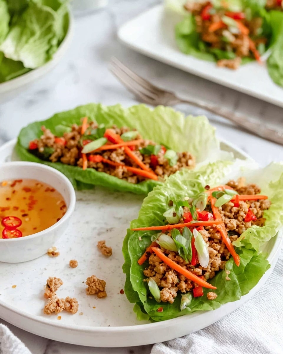 Two lettuce wraps are placed side by side on a white plate with a white marbled texture. Each wrap has a base layer of crisp, bright green lettuce leaves, topped with a second layer of light brown cooked ground meat. On top of the meat, there are thin orange carrot sticks scattered, along with sliced green onions and small pieces of red chili peppers, adding pops of color. Around the plate, some bits of the filling have fallen off. In the background, more lettuce wraps appear, arranged on a white rectangular plate. To the bottom right of the main plate, a small white bowl holds a light orange dipping sauce with tiny red chili flakes floating in it. A silver fork lies on the white marbled surface behind the plate. photo taken with an iphone --ar 4:5 --v 7