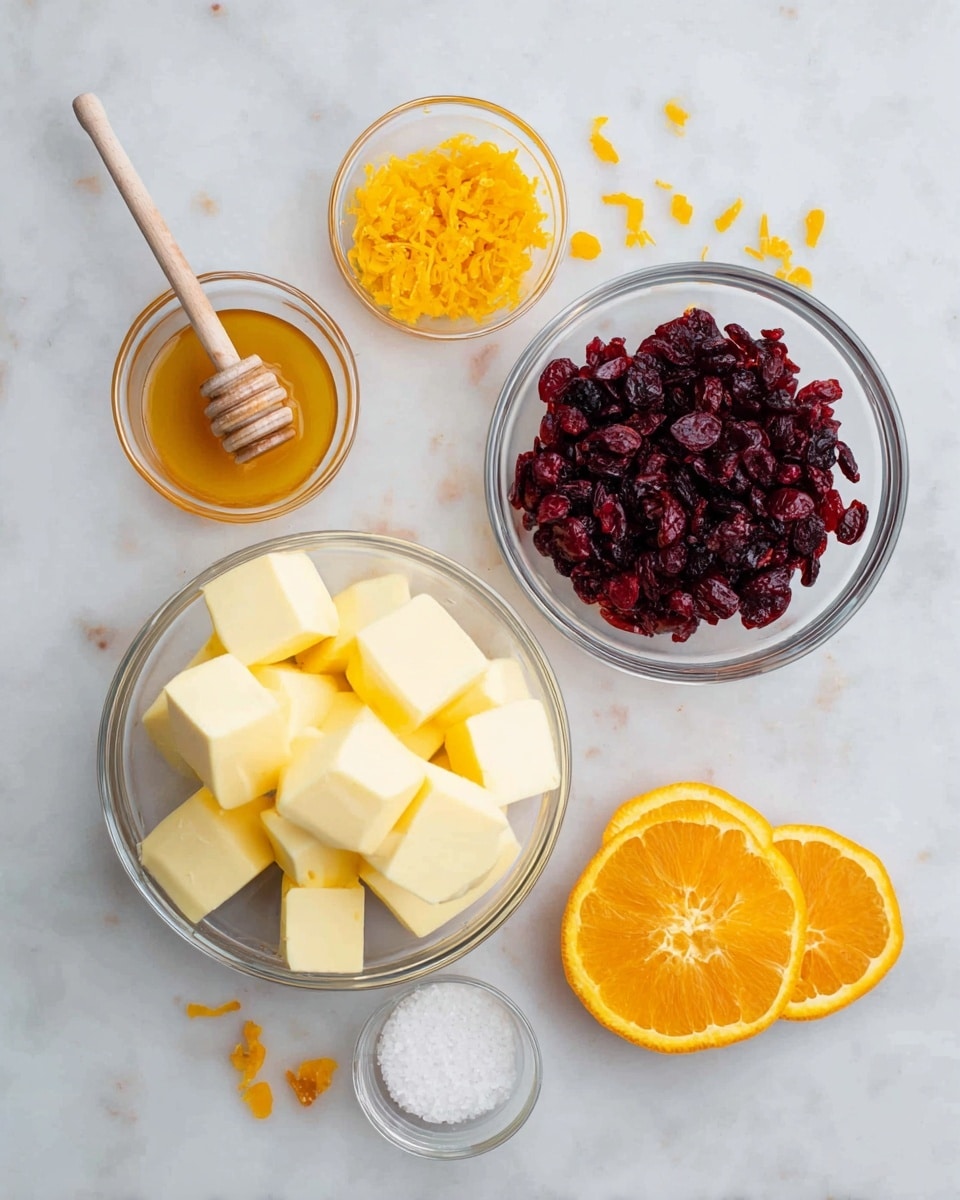 The image shows five clear glass bowls arranged on a white marbled surface. The largest bowl at the bottom left holds many pale yellow cubes of butter. To its right, a medium bowl is filled with dark red dried cranberries with a rough texture. Above the dried cranberries, there is a small bowl containing bright orange lemon zest. Next to the butter bowl on the left, a small bowl holds golden honey with a yellow honey dipper resting inside it. Two orange halves with a bright orange color and detailed segments are placed near the bowls, one at the top center and the other at the bottom right. A tiny bowl with white salt sits below the butter bowl, and small bits of orange zest and dried cranberries are scattered on the surface around the bowls. photo taken with an iphone --ar 4:5 --v 7