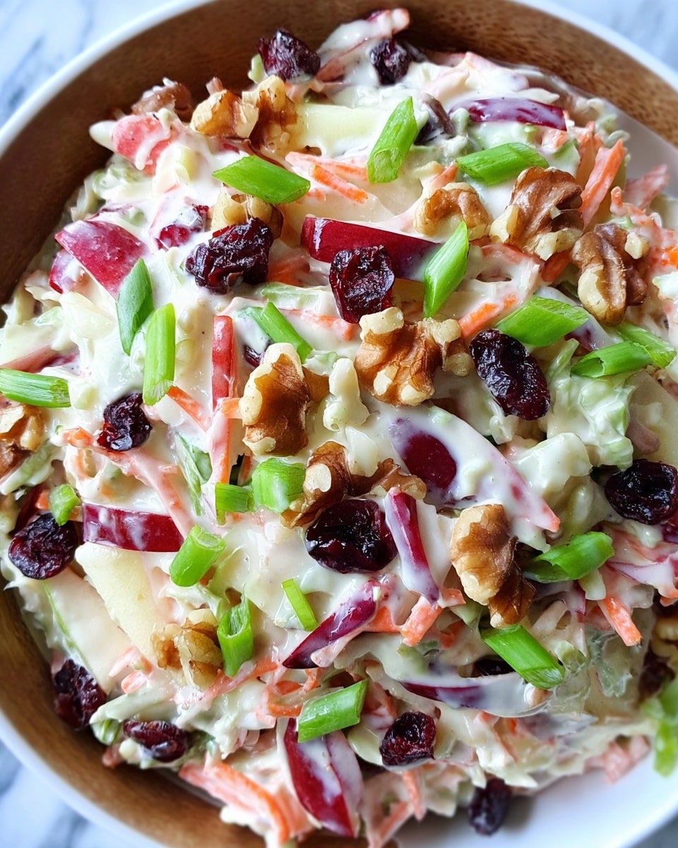A close-up view of a creamy salad in a white bowl with visible layers of chopped apples with red skin, shredded carrots and cabbage mixed in a white creamy dressing, topped with pieces of dark red dried cranberries, bright green chopped green onions, and light brown walnut pieces, all set against a white marbled surface photo taken with an iphone --ar 4:5 --v 7