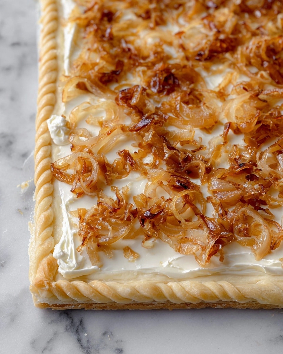 The image shows a square pastry with three visible layers. The bottom layer is light beige dough, flat and smooth, forming the base. The middle layer is creamy white cheese spread evenly across the pastry. The top layer consists of caramelized onions, golden brown with a shiny, slightly oily texture, scattered unevenly over the cheese. The edge of the pastry has a twisted braided border made of the same light beige dough. The pastry is placed on a white marbled surface. photo taken with an iphone --ar 4:5 --v 7