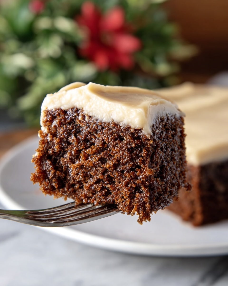 A close-up view of a moist, dark brown single-layer cake piece held by a silver fork. The cake has a soft and crumbly texture with small, even tiny holes throughout. On top, there is a light tan, smooth, and creamy frosting that slightly drapes over the edges. The background shows the rest of the square cake with the same frosting on a white plate, all set on a white marbled surface. In the back, a blurred green and red floral decoration adds a soft touch of color. Photo taken with an iphone --ar 4:5 --v 7