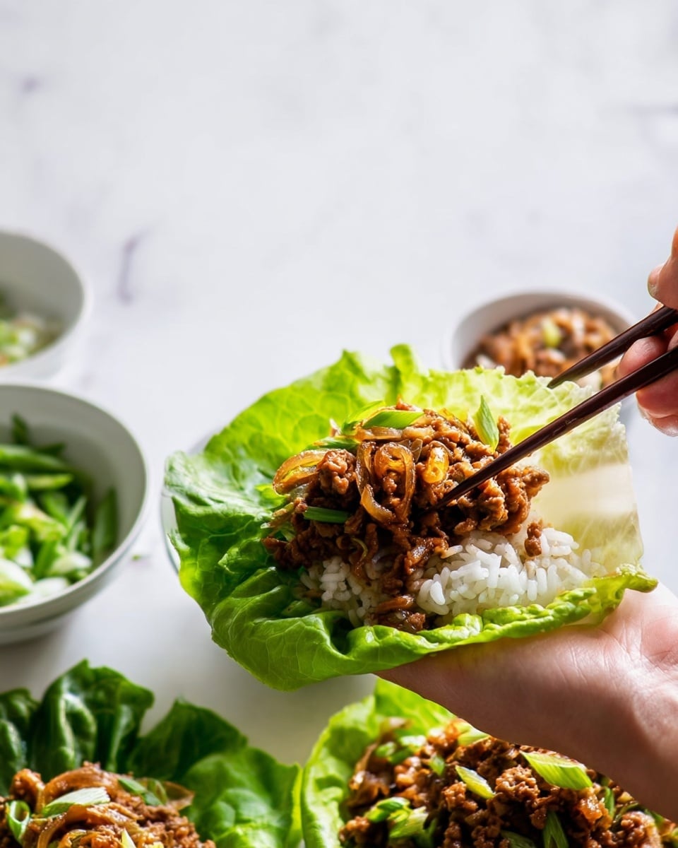 A woman's hand holds a fresh, bright green lettuce leaf shaped like a small bowl, filled with a base layer of white rice. On top of the rice, there is a layer of cooked meat mixed with cooked light brown onions and small green bits, creating a rich, textured look. Above the lettuce and rice, a pair of chopsticks held by a woman's hand is placing more of the meat and onion mixture onto the leaf. In the background, there are white bowls with chopped green vegetables and more lettuce leaves on a smooth white marbled surface. The scene is bright and clean, with natural lighting that highlights the freshness and texture of the food. photo taken with an iphone --ar 4:5 --v 7