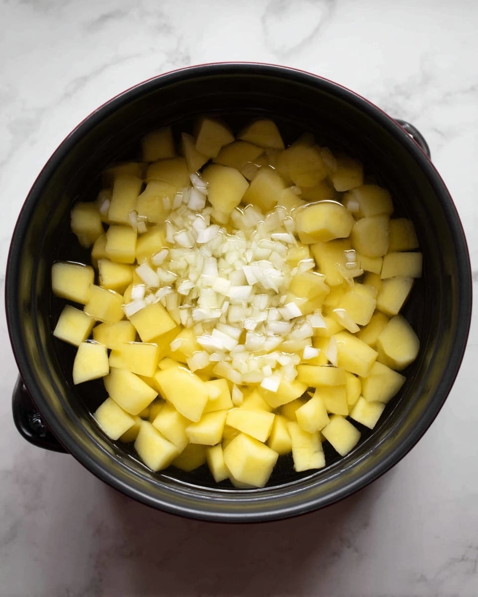 A black pot filled with a layer of yellow potato cubes submerged in clear water, with small pieces of white onion scattered on top in the center. The pot is placed on a white marbled surface. photo taken with an iphone --ar 4:5 --v 7