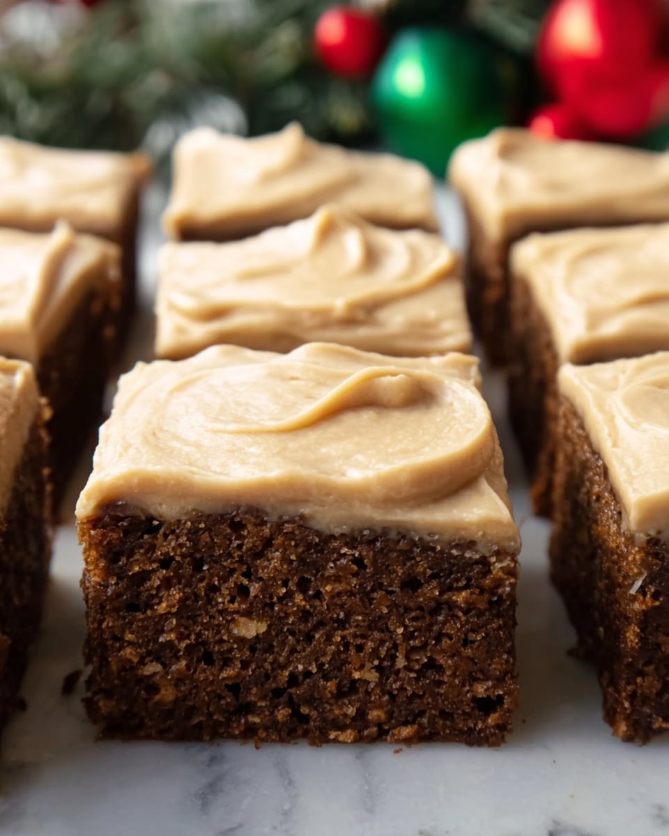 The image shows six square pieces of dark brown cake arranged close together. Each cake piece has one thick layer of smooth, creamy, light tan frosting on top. The texture of the cake looks soft and slightly crumbly, with small holes and bits visible in the cake layer. The frosting is spread evenly with soft swirls and rounded edges on each piece. The background features blurred green and red holiday decorations on a white marbled surface. photo taken with an iphone --ar 4:5 --v 7