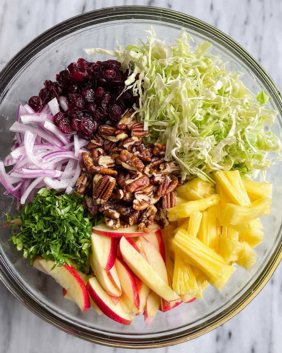 A clear glass bowl filled with neatly arranged layers of fresh salad ingredients, placed on a white marbled surface. At the top right, there is a pile of light green shredded cabbage, next to it on the top left, dark red dried cranberries are placed. Below the cranberries on the left are thin slices of purple onion, beside them at the bottom left is a small bunch of chopped fresh green herbs. In the middle of the bowl, a mound of toasted pecans is present, surrounded on the right by short sticks of yellow pineapple and red apple slices, which extend to the bottom right corner. The overall arrangement is colorful, clean, and fresh-looking. Photo taken with an iphone --ar 4:5 --v 7
