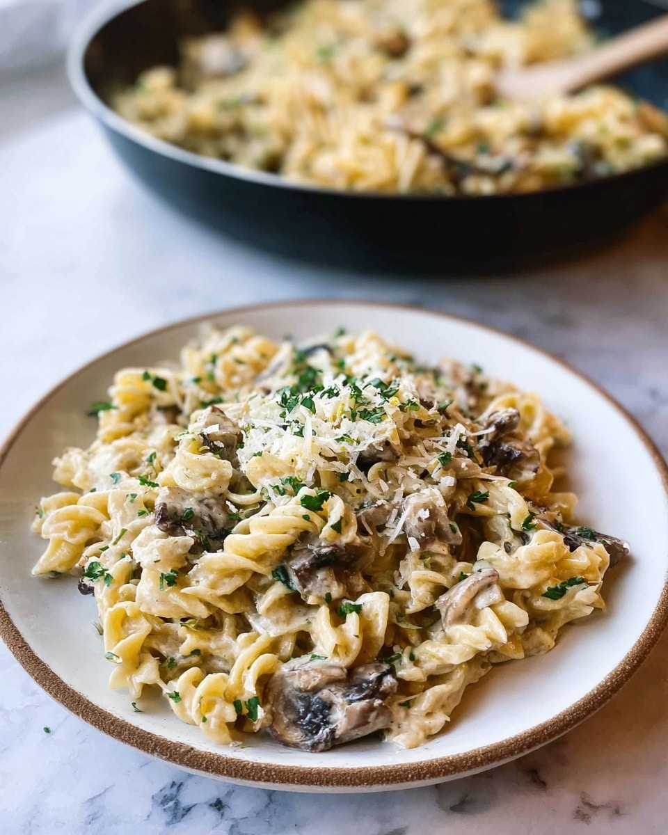 A close-up view of a large black pan filled with creamy pasta. The pasta is light beige with a smooth, slightly curly shape. Mixed in are dark brown mushroom slices. The dish is topped with finely chopped green herbs and a sprinkling of grated cheese that adds a light, powdery texture on top. The background is a white marbled texture. photo taken with an iphone --ar 4:5 --v 7