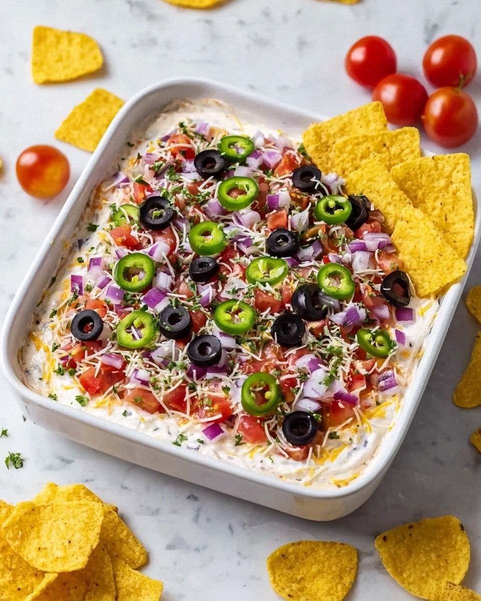A square white dish holds a layered dip starting with a creamy, smooth white base spread evenly at the bottom. On top is a thick layer of finely chopped red tomatoes and small pieces of purple onions, scattered across the surface. Sliced black olives and green jalapeño rings are spread evenly over the tomatoes and onions. A light sprinkling of shredded white cheese and tiny green herb bits cover the entire top, adding texture and color. Four yellow tortilla chips are placed upright along the right inside edge of the dish. The dish sits on a white marbled surface with a few scattered yellow tortilla chips and three small red tomatoes nearby. Photo taken with an iphone --ar 4:5 --v 7