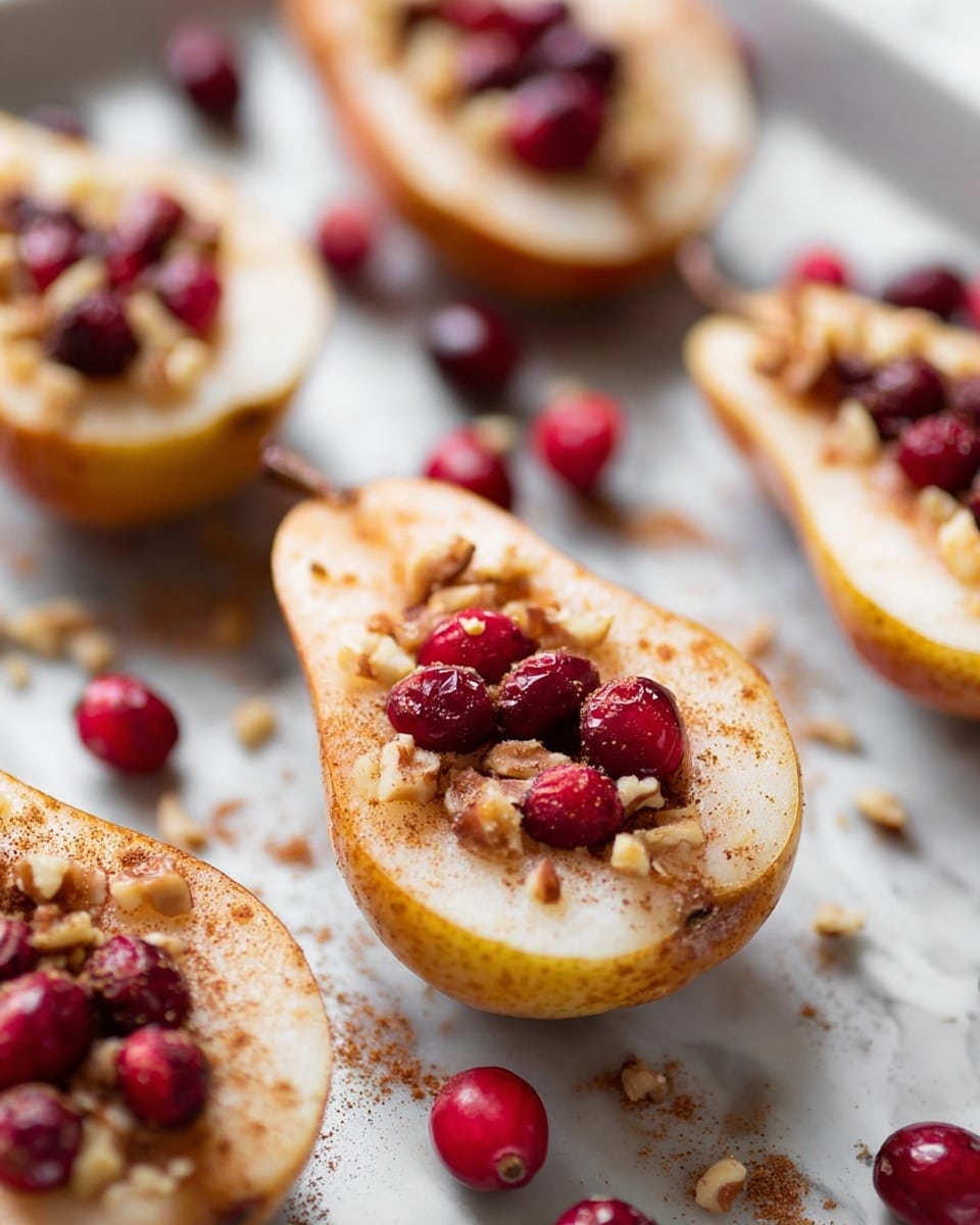 The image shows several pear halves placed on a white marbled surface. Each pear half has a light yellowish-brown skin with the inside flesh pale cream colored. In the hollow center of each pear, there are bright red cranberries surrounded by a topping of chopped nuts and a sprinkle of brown cinnamon powder scattered across the pears and surface. The pears are arranged in a slightly scattered way, with a soft focus on the background showing more pear halves. The texture looks fresh and slightly moist, with the nuts adding a rough, crunchy detail atop the smooth pear flesh. Photo taken with an iphone --ar 4:5 --v 7