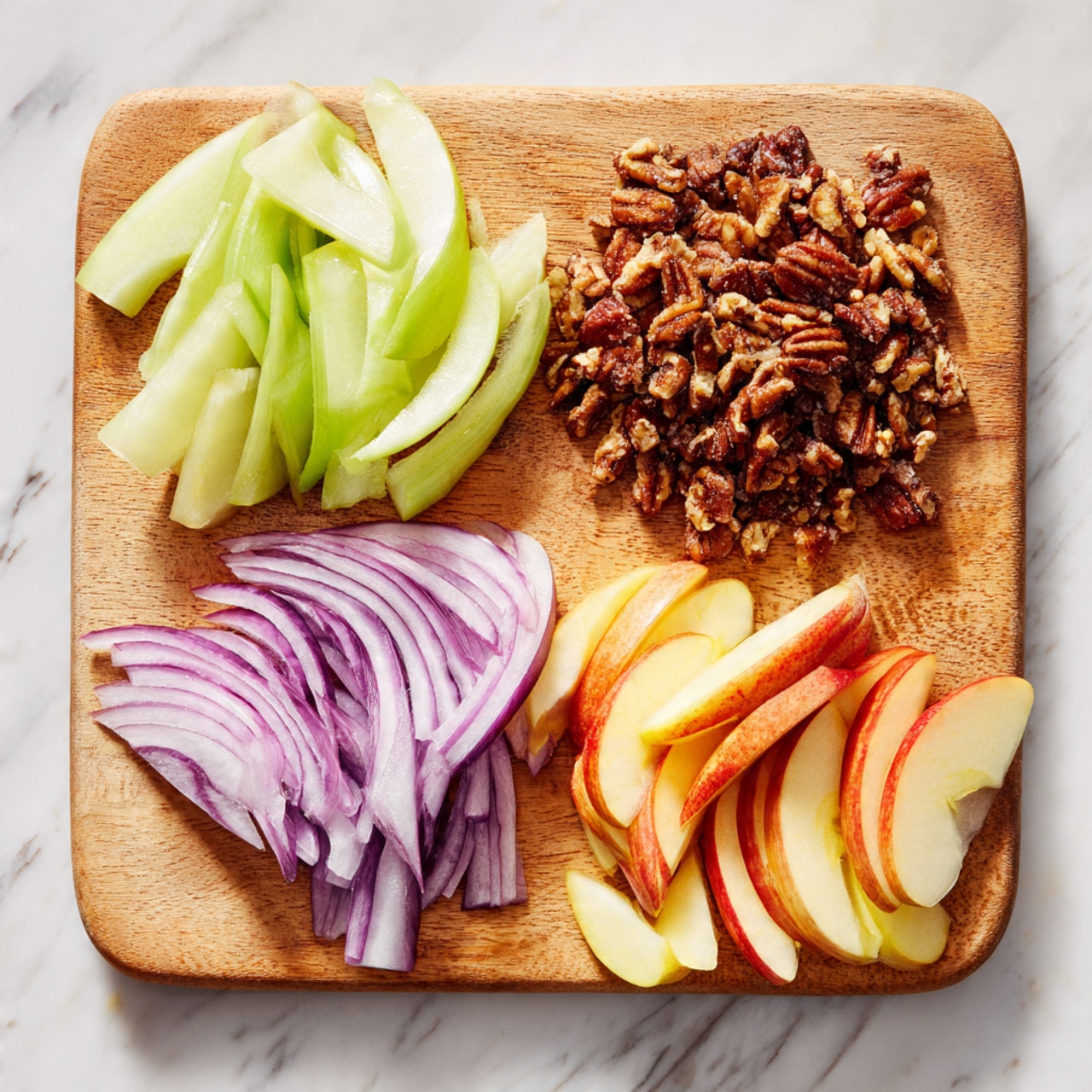 A wooden cutting board is placed on a white marbled surface and holds four different sliced ingredients arranged in separate groups. On the top left, there are pale green curved slices of celery, next to a pile of crumbly, dark brown pecan nuts on the right side. Below the celery on the lower left are thinly sliced purple-red onion strips. On the bottom right, there are thin, long slices of red and yellow apples with the skin still on, fanning out neatly. The overall look is fresh and colorful with a natural texture. Photo taken with an iphone --ar 4:5 --v 7