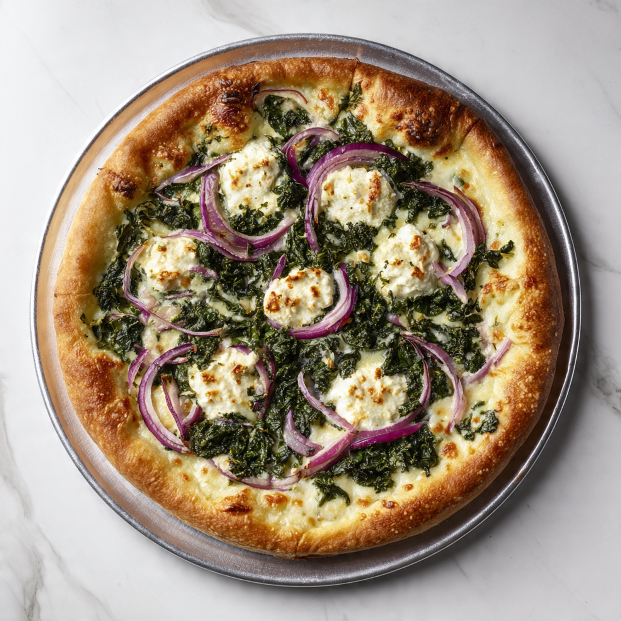 A pizza with a golden brown thick crust sits on a round metal tray. The base layer is melted white cheese spread evenly. On top of this is a layer of finely chopped dark green spinach, covering most of the pizza. Scattered over the spinach are small groups of creamy white cheese dollops that are slightly browned on top. Thin, curved slices of purple-red onion are spread evenly across the pizza, adding a pop of color. The whole scene is set on a white marbled surface. Photo taken with an iphone --ar 4:5 --v 7