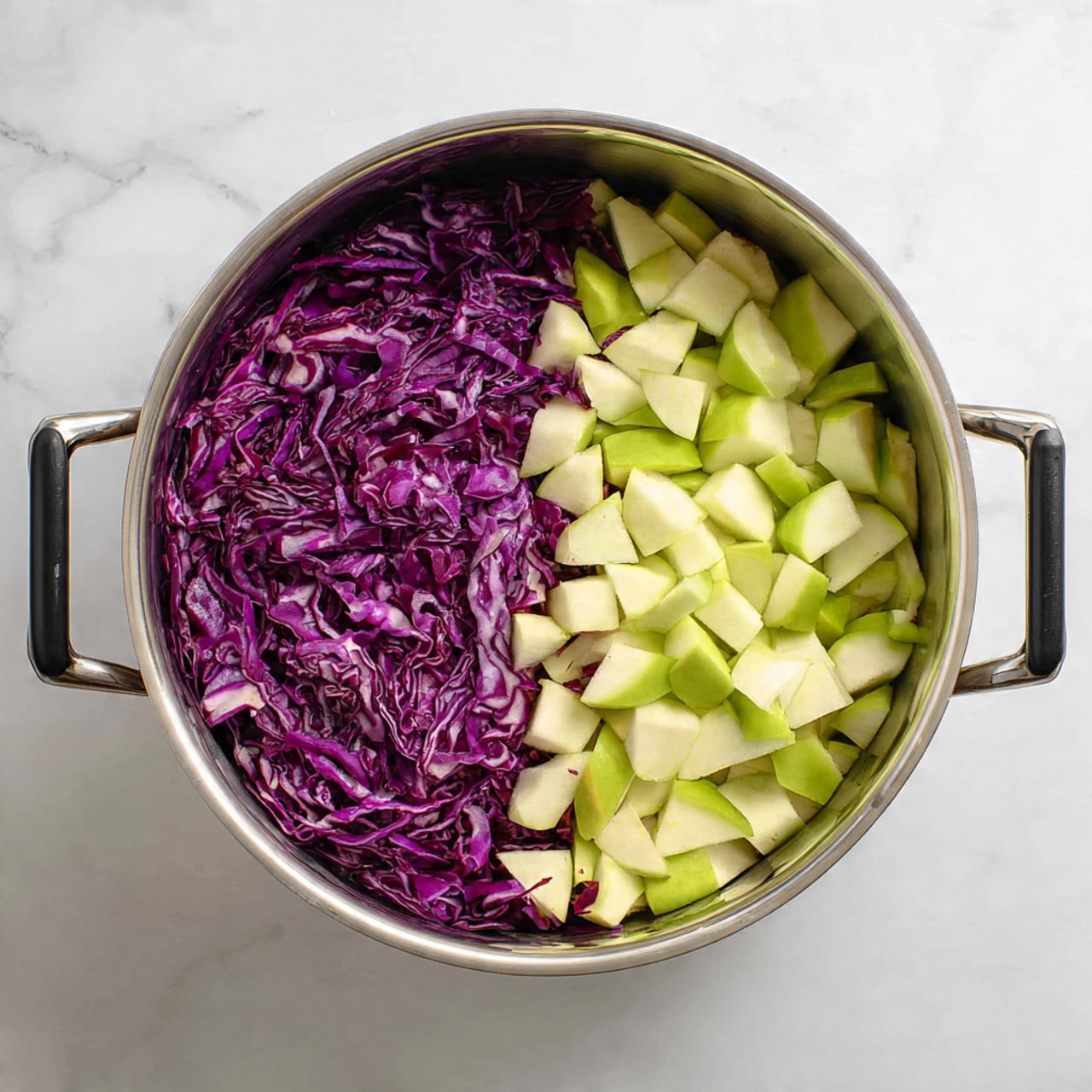 The image shows a round stainless steel pot with two black handles, placed on a white marbled surface. Inside the pot, there are two clear layers of chopped vegetables: one half is filled with thinly shredded purple cabbage with a slightly shiny texture, and the other half holds small chunks of light green and white apple pieces with smooth skin and crisp edges. The vegetables are fresh and neatly separated, filling the pot evenly without mixing. Photo taken with an iphone --ar 4:5 --v 7