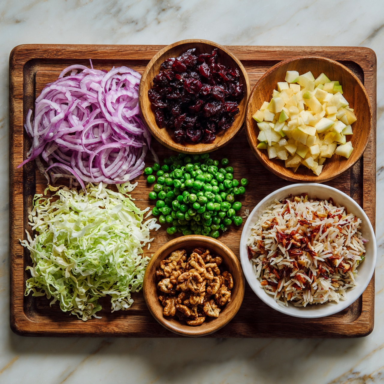 A wooden cutting board sits on a white marbled surface, holding six different food items arranged neatly: thinly sliced purple onion in a pile on the top left; a small wooden bowl filled with dark red dried cranberries at the top center; small pale yellow diced pieces of fruit, likely apple, on the top right; bright green peas scattered in the center; shredded pale green cabbage on the bottom left; a small wooden bowl of brown roasted nuts near the bottom center; and a white bowl filled with a mix of cooked multi-colored rice on the bottom right. Photo taken with an iphone --ar 4:5 --v 7