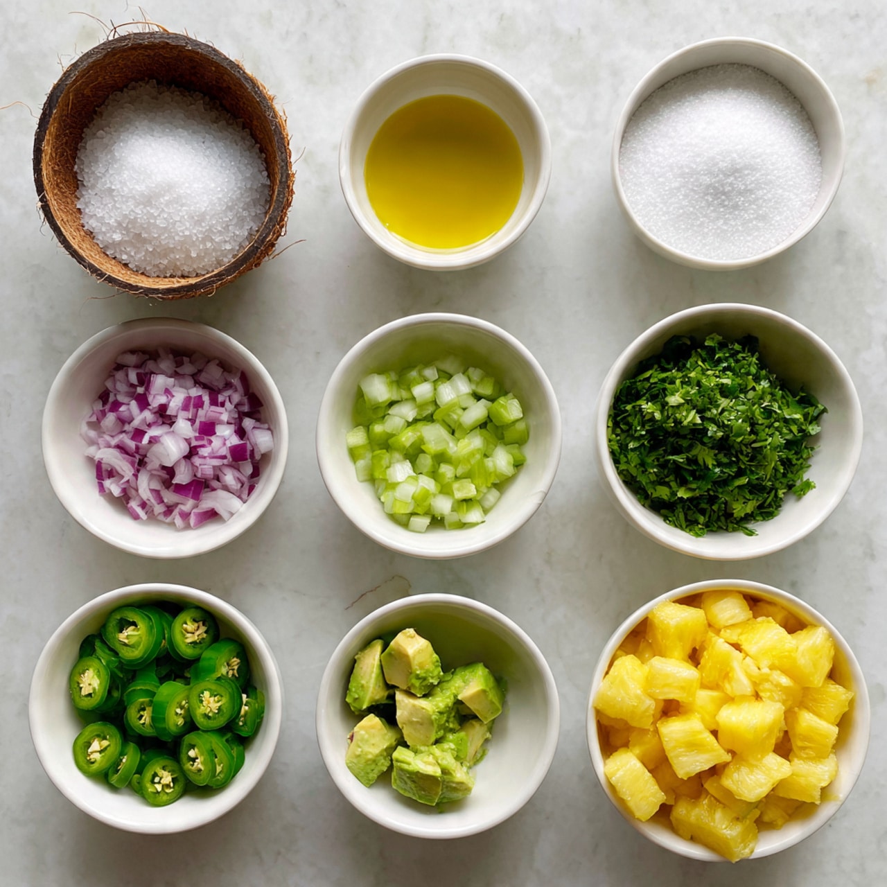 The image shows a neat arrangement of nine white bowls on a white marbled surface. Starting from the top left, the first bowl looks like a half coconut shell filled with coarse salt, next to it is a small white bowl with golden oil, followed by a bowl filled with white granulated sugar, and a bowl full of finely chopped green herbs. Below these, from left to right, there is a bowl with finely chopped red onions, a bowl with small green cucumber cubes, and a bowl with finely chopped bright green jalapeños. At the bottom there is a small bowl with a clear liquid, a bowl with diced green avocado, and the largest bowl filled with diced yellow pineapple pieces. The overall colors are fresh and vibrant, with a clean and organized presentation. photo taken with an iphone --ar 4:5 --v 7