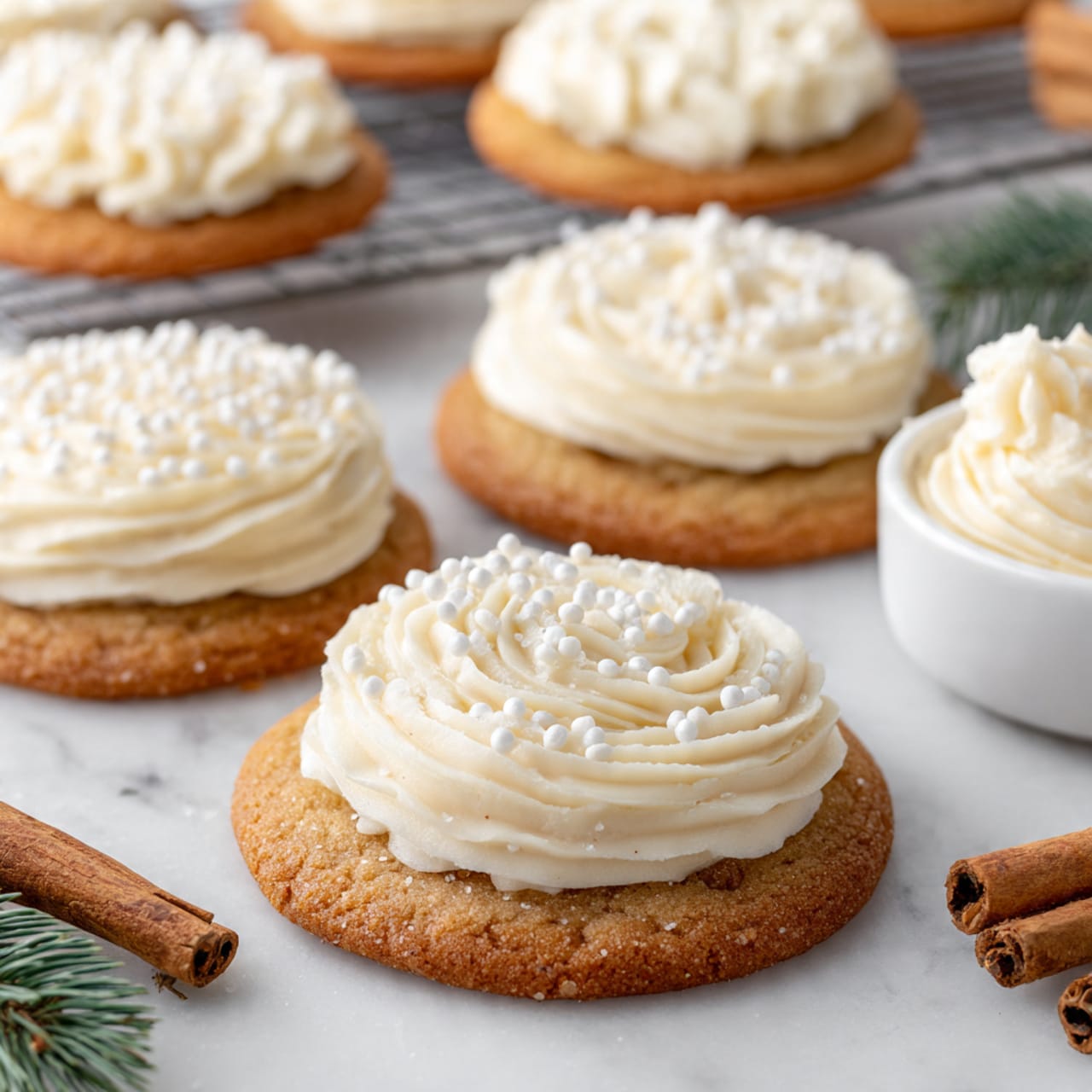 The image shows round sugar cookies on a white marbled surface, each topped with two layers: a light golden brown cookie base with a slightly rough texture, and a thick layer of piped creamy white frosting on top. The frosting is applied in different patterns, including swirls, dollops, and lines, giving variety to each cookie’s look. Some cookies have small white sugar sprinkles on the frosting that add a bit of texture. In the background, more cookies are placed on a metal cooling rack, and on the right side, there is a white bowl holding additional frosting. There are cinnamon sticks and a small sprig of green pine at the edges, enhancing the cozy feel. Photo taken with an iphone --ar 4:5 --v 7