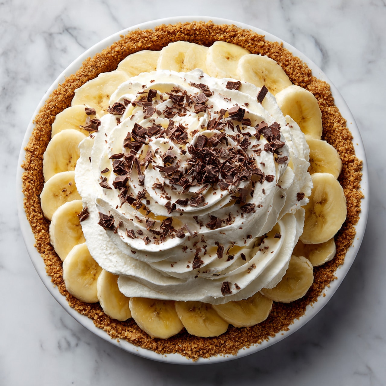 A pie with three visible layers sits on a white marbled surface. The bottom crust is golden brown and crumbly, pressed evenly around the pie dish. Above the crust, slices of light cream-colored banana form the second layer. The top layer is a large swirl of fluffy white whipped cream, sprinkled with small shavings of dark brown chocolate, adding texture and contrast. The entire pie has a fresh and inviting look. Photo taken with an iphone --ar 4:5 --v 7
