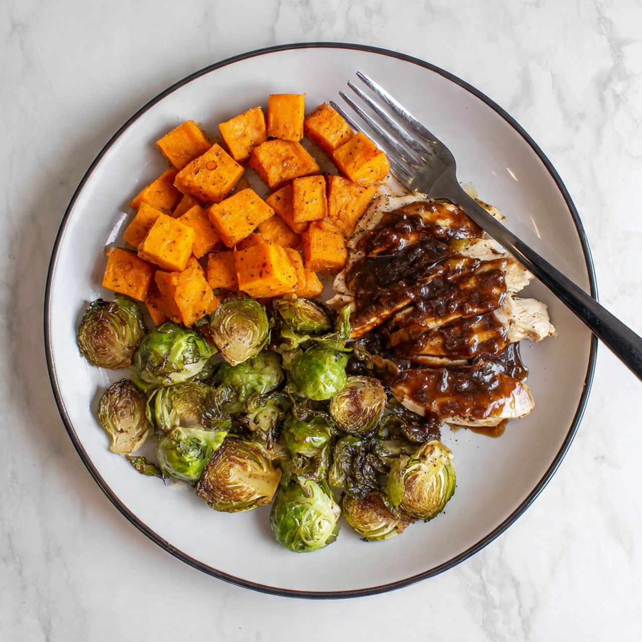 The image shows a white tray with three sections of food arranged from left to right: roasted Brussels sprouts, cooked white chicken pieces topped with a dark red sauce, and cubed roasted orange sweet potatoes. The Brussels sprouts are browned on the edges, the chicken pieces are light with seasoning and covered with thick dark red sauce that looks like a berry glaze, and the sweet potatoes have a warm, soft texture with some light browning. A spoon with some sauce rests near the bottom chicken piece. The tray is on a white marbled surface. photo taken with an iphone --ar 4:5 --v 7