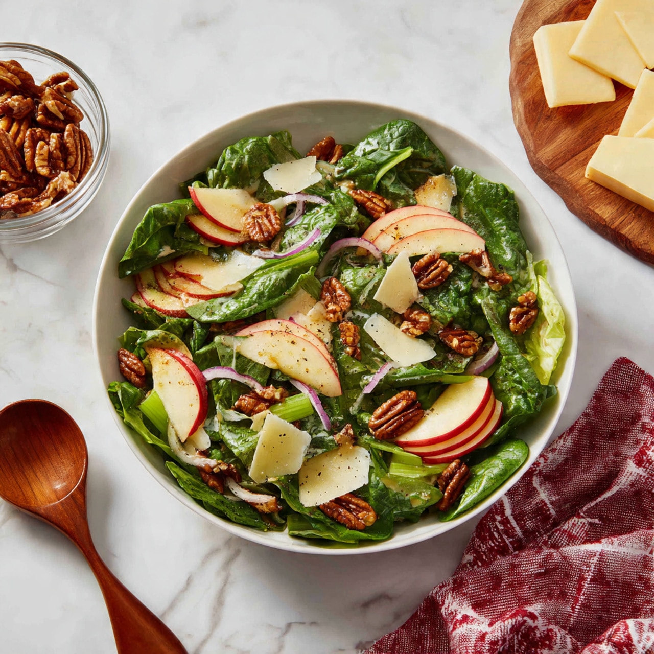 A white bowl filled with layers of fresh salad ingredients, starting with a base of mixed green leafy lettuce and spinach at the bottom. On top of the greens, there are four separate sections: one with chopped light green celery pieces, another with small chunks of brown walnuts, a third with thin slices of red and yellow apple, and the last section has thinly sliced purple onions. A woman's hand is holding a silver measuring cup pouring dark brown dressing over the salad. The bowl sits on a white marbled surface. photo taken with an iphone --ar 4:5 --v 7