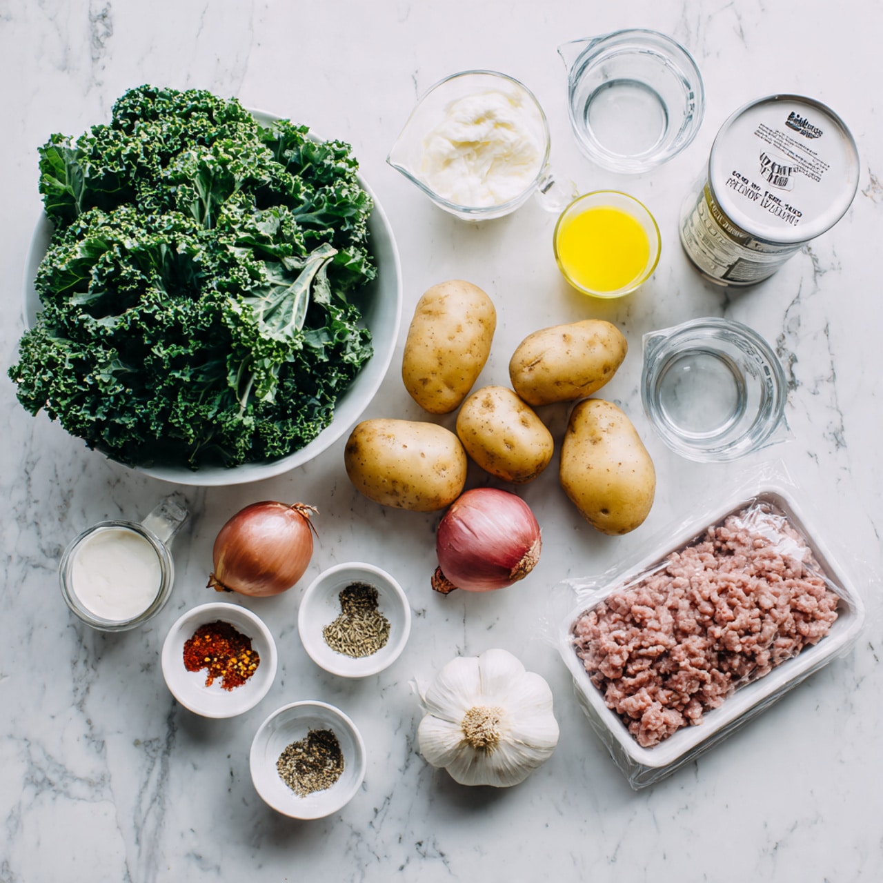 The image shows various cooking ingredients arranged neatly on a white marbled surface. On the left, there is a white bowl filled with bright green kale leaves. Next to it are three small potatoes in red, pink, and brown colors. Above them are clear measuring cups with water and cream, and a yellow liquid in a plastic cup. To the right, a small white can with a label of white beans, a whole onion, and a tray holding raw light brown ground meat partially wrapped in clear plastic are visible. In front of the bowl and potatoes are two small white bowls with spices, one containing a mix of red pepper flakes, salt, and black pepper, and the other with a red powder. A couple of garlic cloves sit near the measuring cups. The clean, bright arrangement emphasizes the fresh ingredients in a simple, clear way photo taken with an iphone --ar 4:5 --v 7