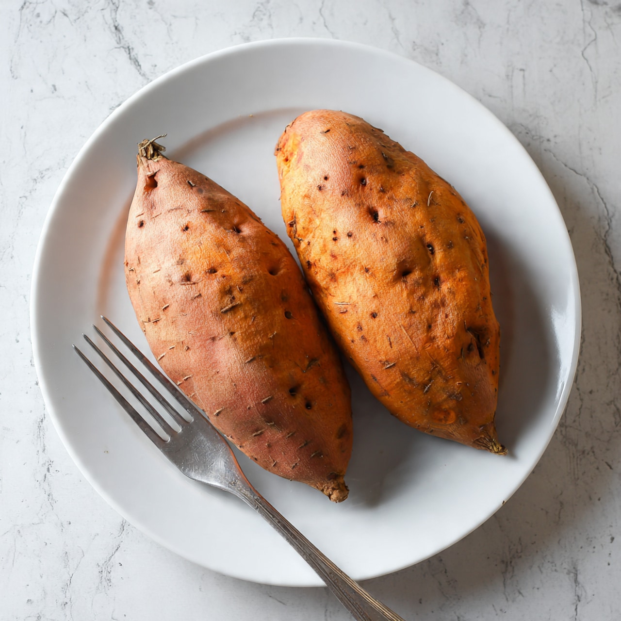 Two whole baked sweet potatoes with light brown skin and small holes in the skin are placed side by side on a round white plate. A silver fork is positioned at the bottom left, touching the lower sweet potato. The plate is on a white marbled surface with subtle gray veins. The lighting is soft and natural, highlighting the textures of the sweet potatoes and the plate. photo taken with an iphone --ar 4:5 --v 7