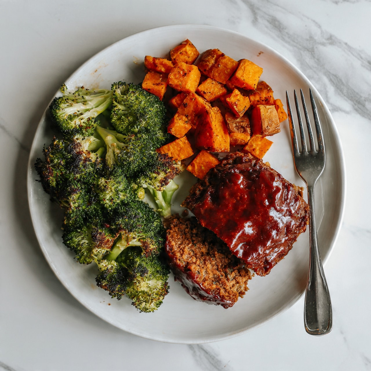 A dark gray baking tray holds three sections of food evenly spaced: on the left, a layer of small orange cubes with a slightly rough texture fills about one-third of the tray; in the middle, two round patties covered with a shiny dark brown glaze sit side by side with some light brown sauce bubbling around their edges; on the right, green broccoli florets with lightly roasted tips cover the remaining space. The tray rests on a white marbled surface. photo taken with an iphone --ar 4:5 --v 7