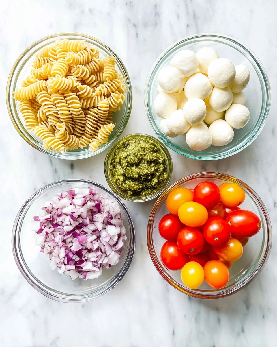 Five clear glass bowls are arranged on a white marbled surface. The top left bowl holds a tight pile of pale yellow rotini pasta, the top right bowl contains smooth white mozzarella balls piled together. The bottom left bowl is full of finely textured green pesto, the small center bowl displays finely chopped red onions with a mix of purples and whites, and the bottom right bowl is filled with round cherry tomatoes in shades of bright red, orange, and yellow, all shiny and smooth. The scene is brightly lit, showing the fresh colors clearly. photo taken with an iphone --ar 4:5 --v 7
