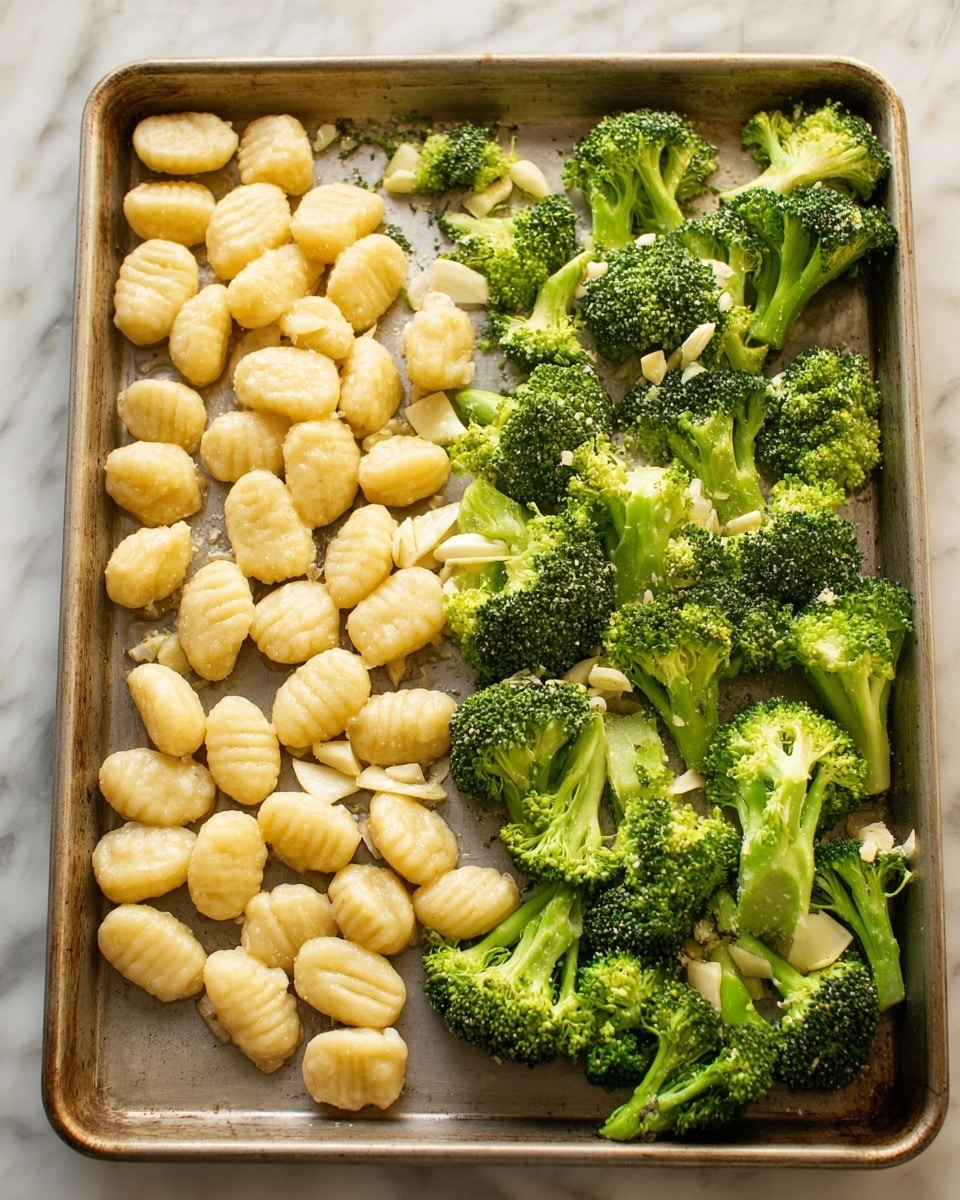 A baking tray holds two main layers of food: on the left side, there is a pile of pale yellow gnocchi, each piece round with small ridges; on the right side, bright green broccoli florets with thick stems are spread out. Both the gnocchi and broccoli have small pieces of chopped garlic sprinkled on top. The tray rests on a white marbled surface. Photo taken with an iphone --ar 4:5 --v 7