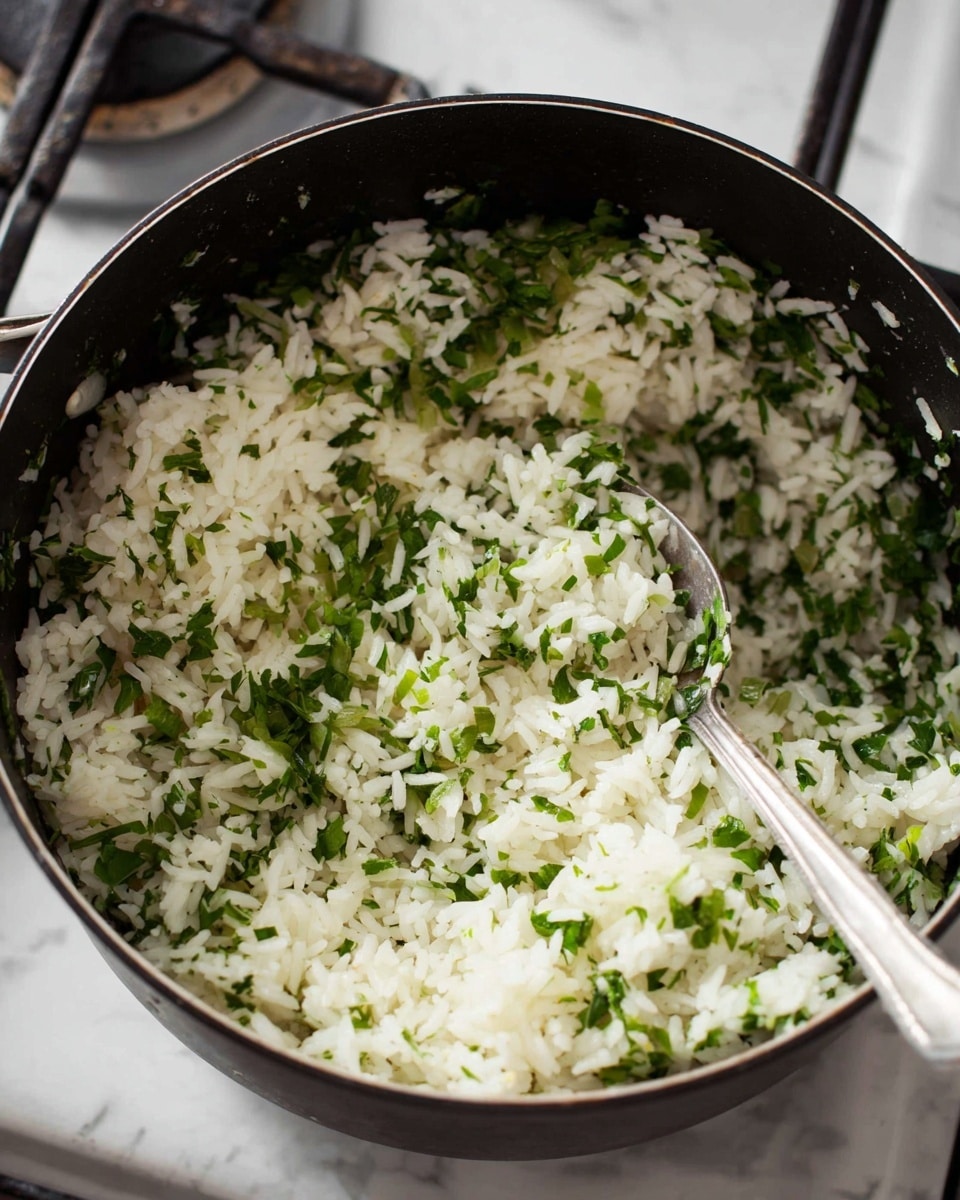 A black pot filled with cooked white rice mixed evenly with finely chopped green herbs, giving a fresh and vibrant look with small green leaf pieces scattered throughout. A silver spoon is placed inside the pot, resting against its edge. The pot sits on a white marbled stove surface. The texture of the rice looks soft and fluffy, and the herbs add a slight texture contrast, making the dish visually appealing. Photo taken with an iphone --ar 4:5 --v 7