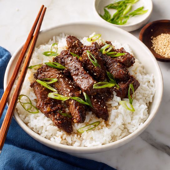 The dish shows a large white bowl filled with many pieces of brown cooked meat scattered evenly across the surface, with small green onion rings spread on top for color and texture. The bowl sits on a white marbled surface with a dark blue cloth napkin loosely placed nearby. In the background, a white bowl contains fluffy white rice with a wooden spatula resting inside. Small dishes nearby hold sesame seeds and green onion slices, adding to the visual story of the meal. The overall scene is bright and clean, with the focus on the rich brown meat and fresh green garnish photo taken with an iphone --ar 4:5 --v 7