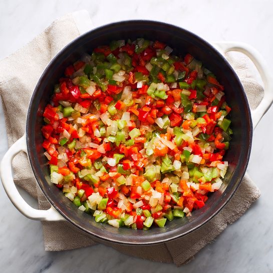 Inside a large black pot with white handles resting on a beige cloth over a white marbled surface, there is a single layer of bright, chopped vegetables. The vegetables are a mix of juicy, diced red bell peppers, finely chopped translucent onions, and small green chili pieces, all lightly cooked and mixed together, revealing a colorful blend of red, white, and green shades. The vegetables have a slightly shiny texture, showing they are sautéed but not overcooked. photo taken with an iphone --ar 4:5 --v 7