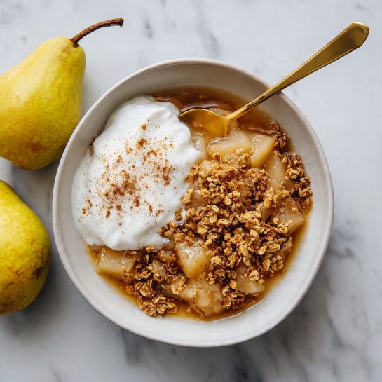 A close-up view of a white bowl filled with a baked fruit crisp, showing a top layer of golden brown oat crumble with a rough, crunchy texture, sprinkled with cinnamon powder. At the center, there is a scoop of white vanilla ice cream melting slightly into the crumble, with cinnamon dusted on top of the ice cream. The edges of the bowl show a bit of the brown juice bubbling underneath the crumble. The bowl is placed on a white marbled surface. photo taken with an iphone --ar 4:5 --v 7