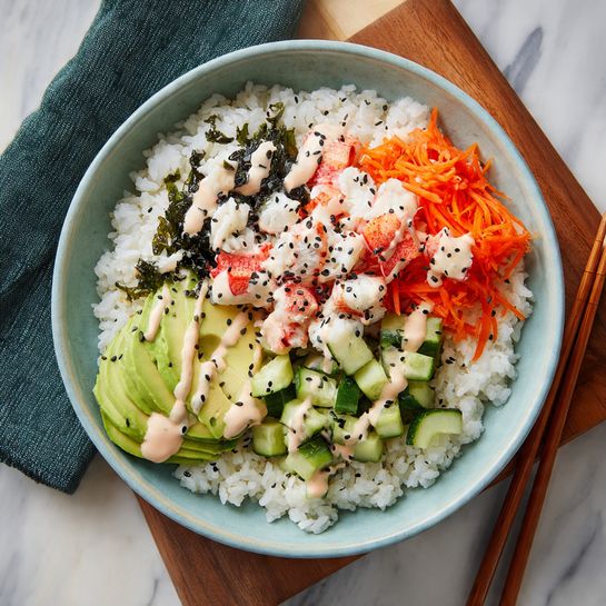 There are four bowls filled with a colorful poke dish arranged on a white marbled surface. Each bowl has a base layer of white rice. On top, there are chopped light green avocado pieces, bright orange shredded carrots, red and white crab meat chunks, small green cucumber cubes, and dark black seaweed strips placed in separate sections. The dish is drizzled with a light pinkish-orange sauce and sprinkled with black and white sesame seeds. Three bowls are light blue with a subtle striped pattern on the outside, and one bowl is white. Wooden chopsticks rest on two bowls, and a small wooden bowl filled with mixed sesame seeds sits near the bottom right. A dark green cloth napkin lies under one bowl. photo taken with an iphone --ar 4:5 --v 7
