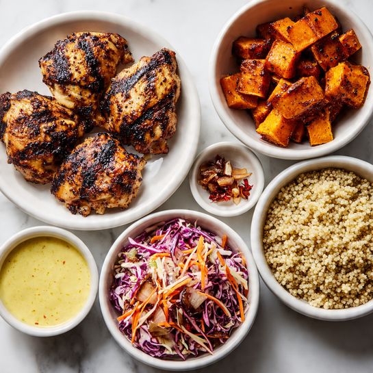 The image shows five white dishes arranged on a white marbled surface. At the center left, a white plate holds three pieces of grilled chicken with dark grill marks and a rich brown color. Above this plate is a white bowl filled with light tan quinoa, showing small grains with a fluffy texture. To the right of the quinoa bowl, another white bowl contains roasted sweet potatoes, cut into chunks with a deep orange color and slightly charred edges. Below the sweet potatoes, a white bowl holds a creamy yellow sauce with small reddish specks. At the bottom, a white bowl is filled with coleslaw made of shredded purple cabbage and thin carrot strips, coated lightly with a dressing. A small white dish with dried shallots is placed near the grilled chicken plate. The photo taken with an iphone --ar 4:5 --v 7