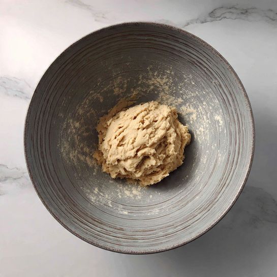 A gray mixing bowl with a rough texture holds a ball of light beige dough with a slightly sticky and uneven surface, resting in the center of the bowl. The background is a white marbled texture. photo taken with an iphone --ar 4:5 --v 7