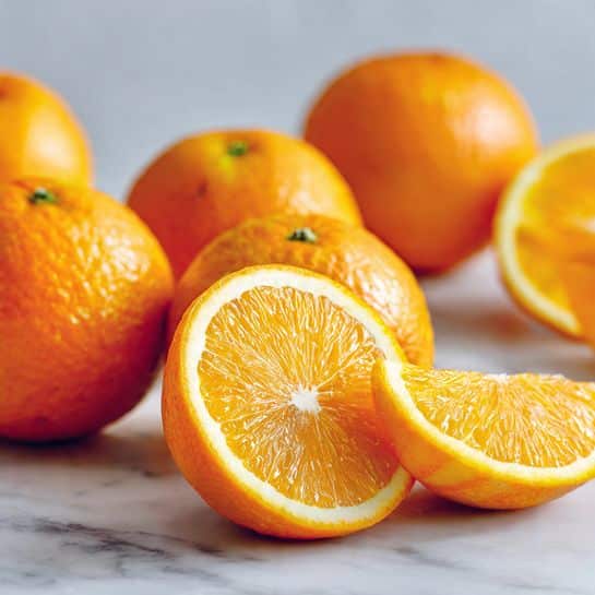 The image shows a white marbled surface with six whole small oranges scattered in the background, each having a bright orange, slightly dimpled skin. In the foreground, there are three thin slices of orange laid flat, showing a light yellow and translucent flesh with a white central core and a thin bright orange peel around each slice. The whole oranges are blurred slightly while the slices are in focus, highlighting their juicy texture. Photo taken with an iphone --ar 4:5 --v 7