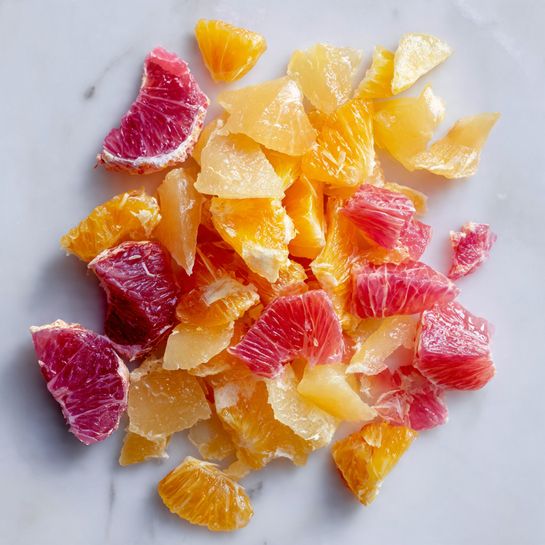 The image shows small pieces of peeled citrus fruits on a white marbled surface. There are two types of fruit pieces: one is a bright yellow-orange color with a smooth, juicy texture and the other is a pinkish-red color with a translucent, slightly rough texture. The yellow pieces are spread mostly on the top right and upper middle parts, while the pink pieces are mostly grouped toward the bottom left. The fruit pieces vary in size and shape, some look like segments, others are smaller bits. The overall scene is clean and bright, highlighting the fresh, juicy look of the citrus pieces photo taken with an iphone --ar 4:5 --v 7