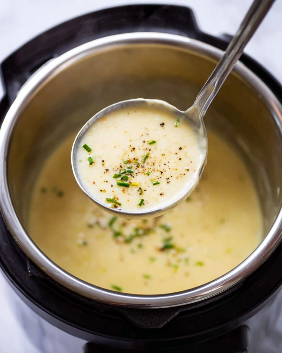 A close-up photo shows a shiny silver ladle holding a thick creamy soup that is pale yellow in color. The soup has small bits of black pepper and chopped green herbs lightly sprinkled on top. The ladle is above a shiny metal pot with more of the same creamy soup inside. The pot is part of a black Instant Pot, which sits on a white marbled surface. Steam rises faintly from the soup, adding a warm and fresh feeling to the scene photo taken with an iphone --ar 4:5 --v 7