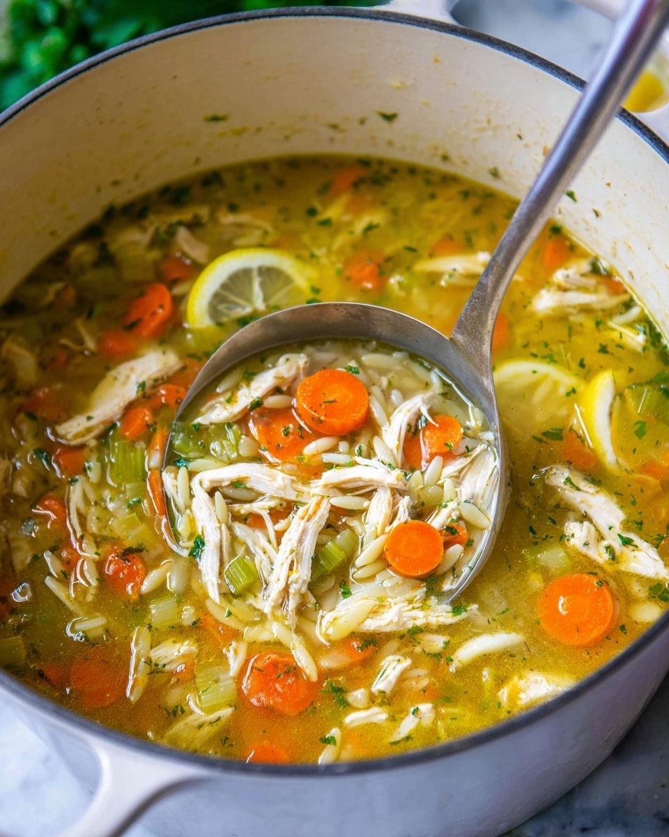 The image shows a large white pot filled with chicken soup containing several layers visible at the top: a clear yellow broth base with small green herb bits scattered throughout, followed by orange round carrot slices and pale green celery pieces. On these vegetables lie many shredded white chicken strips and small white pasta pieces shaped like rice. Two thin lemon slices rest on the soup’s surface adding a touch of bright yellow. A silver soup ladle is partially submerged in the soup, lifting a mix of shredded chicken, pasta, and vegetables, all glistening with the broth. The pot sits on a white marbled surface with some greenery blurred in the background. Photo taken with an iphone --ar 4:5 --v 7