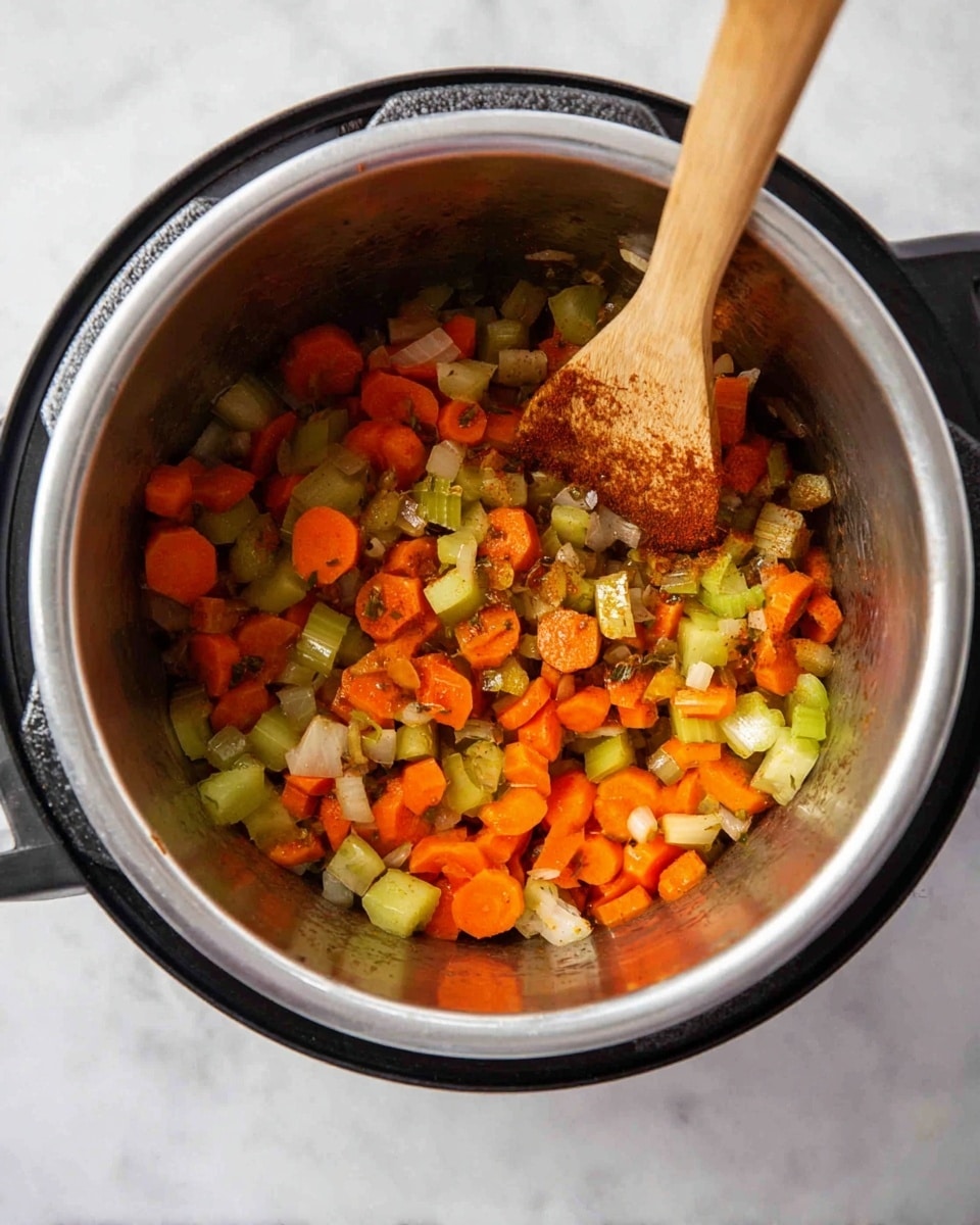 Inside a silver cooking pot, there is a mix of cooked chopped vegetables including orange carrot slices, light green celery pieces, and small white onion chunks. The vegetables look soft and slightly browned, showing some spices on top. A light brown wooden spoon with dark spots rests inside the pot, partly stirring the vegetables. The pot sits on a white marbled surface, and the edges of the black cooking appliance are visible around the pot. photo taken with an iphone --ar 4:5 --v 7